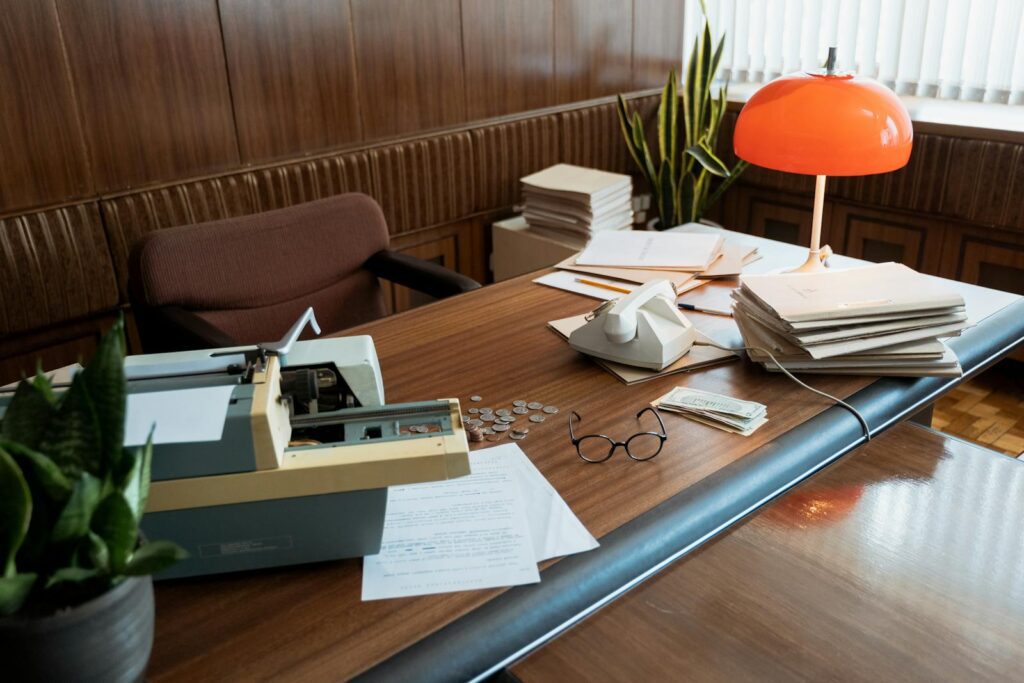 A retro office desk featuring a typewriter, vintage telephone, and stacks of documents.